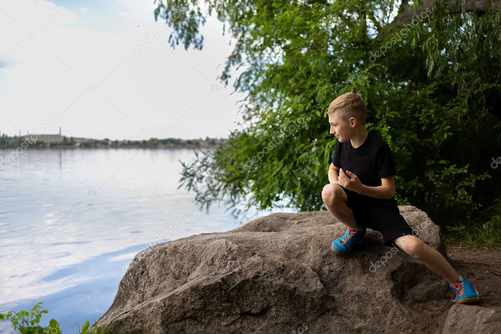 a boy looks into the river sitting on a stone