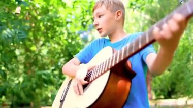 a boy with a guitar in the park pulls the strings