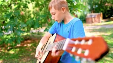 the boy looks at the strings of the guitar and tunes the instrument
