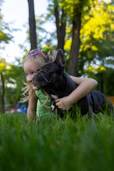 a little girl hid behind a french bulldog, she hugged him and together they look good to the side