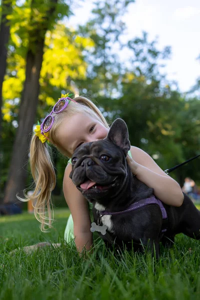 a little girl hugged a french bulldog from behind and rested her head on him
