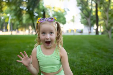 cheerful little girl opened her mouth in surprise and rolled her eyes, she waves her hand in the park