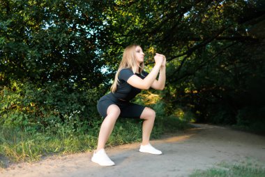 slender blonde girl doing squat exercises in the park