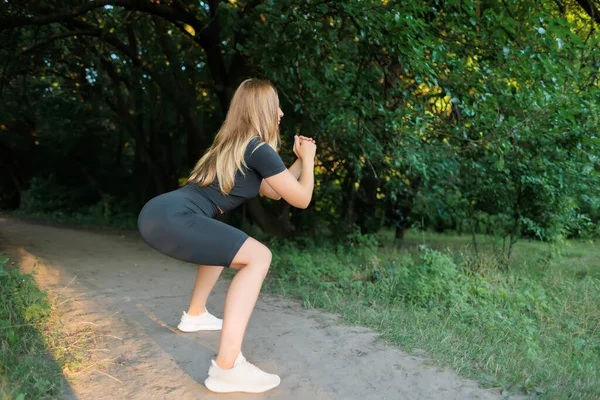 Slender Blonde Park Doing Squats Doing Fitness Outdoors — Zdjęcie stockowe