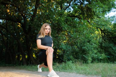 blond sports girl performs elements for stretching the legs, tilting, leaning on the leg and performing stretching