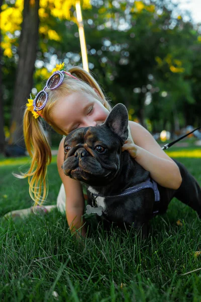 a little girl hugged a french bulldog by the neck and closed her eyes