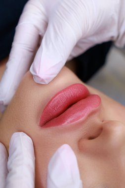 close-up of a permanent make-up of lips made in powder technique, a master in white gloves holds the lips of a model with his fingers