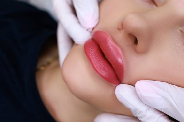 procedure of permanent make-up of the lips with the help of a machine, the master stretches the corners of the lips of the model