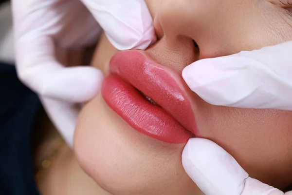 procedure of permanent make-up of the lips with the help of a typewriter, the master gently holds the lips of the model with his fingers