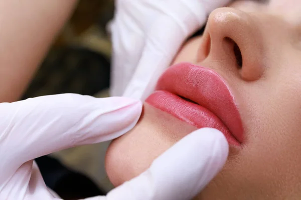 close-up of a permanent make-up master holding the lips of a model showing the completed work of permanent make-up of the lips