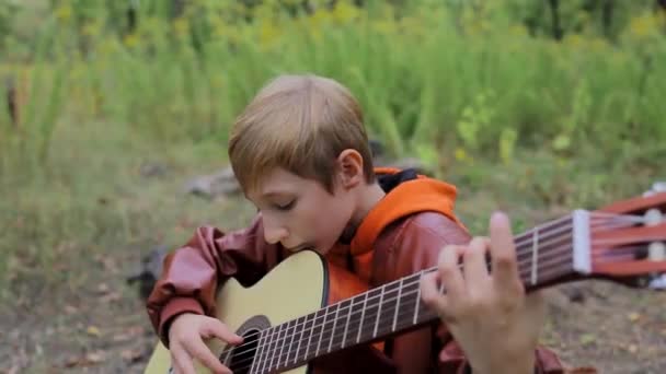 在秋天的森林里 一个男孩手里拿着一把吉他 手里拿着琴弦 — 图库视频影像