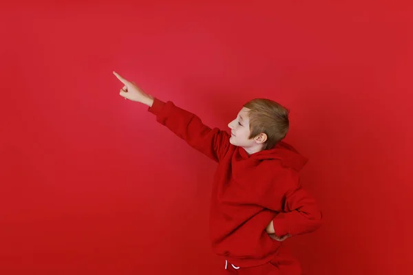 Czerwonym Tle Stoi Chłopiec Ubrany Czerwony Dres Pokazuje Dłoń Boku — Zdjęcie stockowe