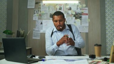 Desperate detective lights a cigarette and ponders sitting at the table in his cabinet. FBI agent, police officer or private detective is stumped by a hard murder investigation.High quality 4k footage