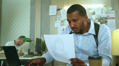 Focused detective comparing missing poster with information in laptop at police department.Handsome policeman doing police paper work, filling reports sitting at the table. High quality 4k footage