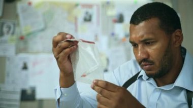 Close up of focused detective examining evidences. Handsome male police officer investigating clues in safe package of complexity homicide case while sitting at police department. 4k footage