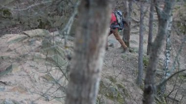 Alone man with backpack hiking in rocky terrain in forest. Alone travelling man in hiking clothes having journey on his own. Outdoor hiking travel concept in nature. High quality 4k footage