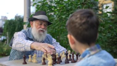 Senior male chess master teaching chess strategy young genius boy. Grandpa and his grandson spending family time studying chess board game.Kid development, gain abstract thinking skills, hobby concept
