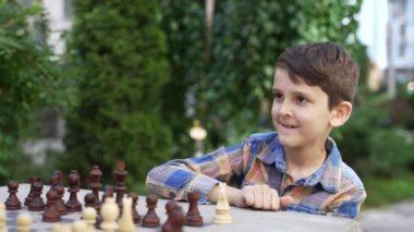 Close up of little genius boy chess player. Brilliant little boy playing chess with his chess master outdoor in the park. High quality 4k footage