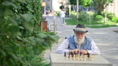 Senior elderly male playing chess on his own outdoor at summer. Retired man spending time playing chess in the street. High quality 4k footage