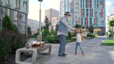 Cheerful granddaughter and grandpa dancing together in the middle of the street. Happy multi-generation family spending time together. High quality 4K footage