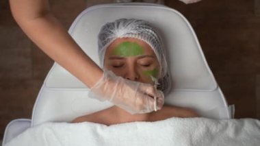 Profesyonel güzellik uzmanının müşterilerin yüzüne fırçayla yeşil maske takması. Güzel bir kadının yüz bakımını yakından takip et. Güzellik kliniği, kaplıca ve cilt bakımı konsepti. 4k görüntü