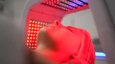 Genç bir bayanın güzellik salonunda kırmızı ve mavi LED ışık yüz terapisi görmesine yakın çekim. Saldırgan olmayan bir tür fototerapi. Güzellik, sağlık ve sağlık konsepti. Kozmetik ve Cilt Bakımı