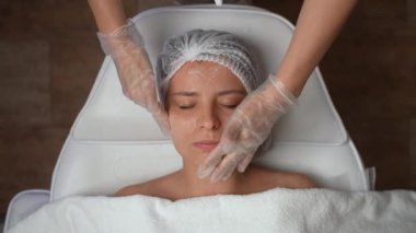 Kozmetik uzmanının kadın yüzüne nemlendirici krem ya da krem sürerken kaplıcada uzanması ve dinlenmesi. Güzellik kliniği, kaplıca ve cilt bakımı konsepti. Yüksek kalite 4K görüntü