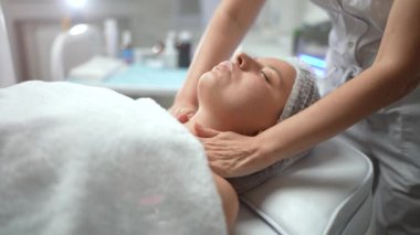 Kozmetik uzmanı, kozmetoloji kliniğindeki kadın müşteriye yüz ve boyun masajı yapıyor. Cerrahi olmayan kozmetoloji, profesyonel cilt bakımı, güzellik tedavi konsepti. Yüksek kalite 4K görüntü
