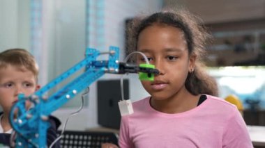 Parlak Afrikalı ilkokul öğrencisi kızın robot vinçinin robot mühendislik laboratuvarında nasıl çalıştığını dikkatle izlemesi. Fütürist teknolojiler bilim sınıfı. STEM 