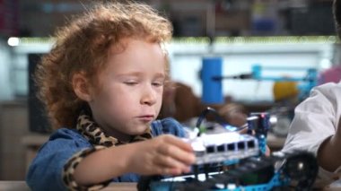  Kızıl saçlı, kıvırcık ilkokul öğrencisinin robot okulu dersinde oynayıp elektrikli oyuncaklar yapmasına yakın çekim. Sınıfta robot montajı yapan bir çocuk. Yüksek kalite 4k görüntü