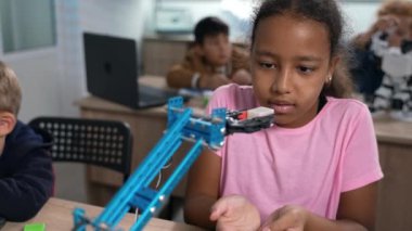 Parlak Afrikalı ilkokul öğrencisi kızın robot vinçinin robot mühendislik laboratuvarında nasıl çalıştığını dikkatle izlemesi. Fütürist teknolojiler bilim sınıfı. STEM 
