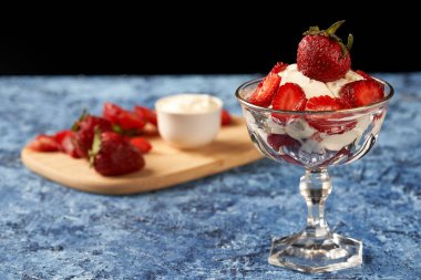 Arkasında çilek tahtası olan çilek ve krema bardağı.