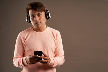 Kulaklıklı, cep telefonlu, gri arka planda ve pembe elbiseli Latin bir adam.