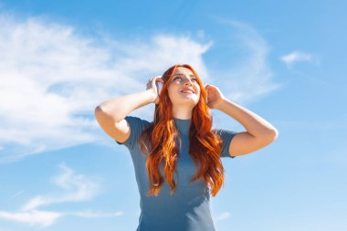 Kablosuz kulaklıklarla müzik dinleyen ve gökyüzüne fotokopi aletiyle bakan sevimli genç bir kadın.. 