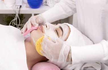 Güzellik uzmanının elleri yüz temizleme ürününü süngerle, cilt bakımı konseptiyle, yakın çekim detaylarıyla temizliyor.