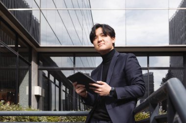 İş yerinin dışındaki Asyalı adam tabletini tutuyor ve gülümsüyor. Yüksek kalite fotoğraf