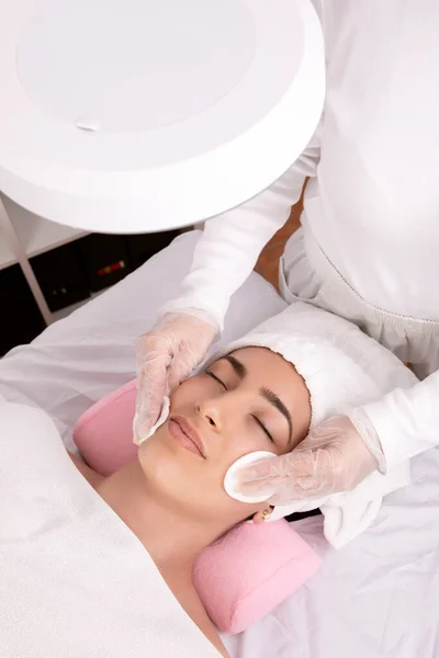 hands of Esthetician performing facial cleansing, applying tonic with cotton pads, skin care concept, closed detail shot. High quality photo