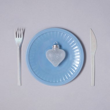 Çatal ve bıçak arasında mavi tabakta takılabilen Xmas kalp şeklinde. Gri arka planda buzlu kompozisyon. Minimalist Noel ve Yeni Yıl konsepti. Yaratıcı soğuk kış düzlüğü fikri.