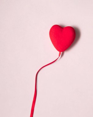 Kırmızı kalp, pastel açık pembe arka plandaki bir balon gibi uçup gidiyor. Modern Sevgililer Günü konsepti. Yaratıcı aşk fikri.