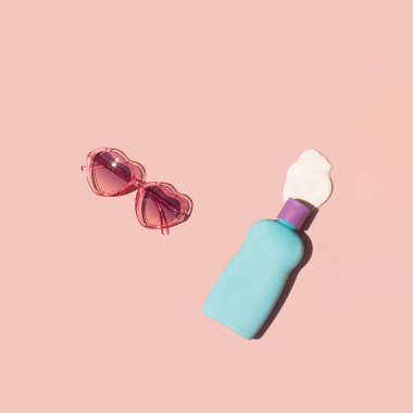 Pastel açık pembe arka planda güneş gözlüğü ve güneş koruyucu krem. Minimalist yaz konsepti. Güneşli gün kompozisyonu. Plaj ilhamı için hazır.