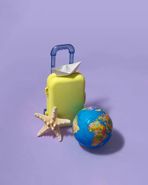Minimal travel the world composition. Suitcase and globe on pastel light purple background. Creative summer holiday concept.
