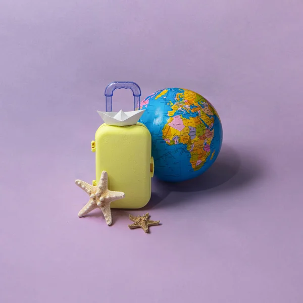 Minimal travel the world composition. Suitcase and globe on pastel light purple background. Creative summer holiday concept.