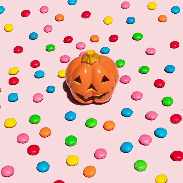 Halloween holiday concept. Scary pumpkin and candies on pastel pink background. Minimal holiday composition.