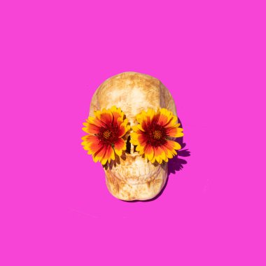 Halloween holiday concept. Scary skull with orange flowers on bold purple background. Minimal festive composition.