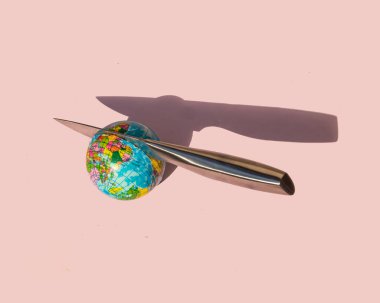 Minimalistic environment concept. Knife cutting globe on pastel light pink background. Creative ecological composition. Political idea.