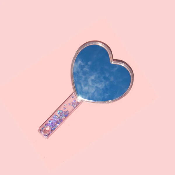 Modern composition with heart shaped mirror and blue sky reflection on pastel light pink background. Creative love concept. Creative Valentine\'s day idea.