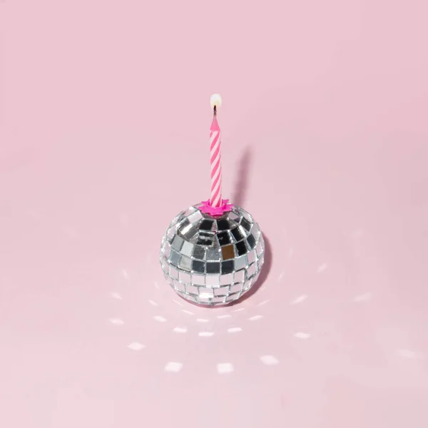 Shiny disco ball and candle on pastel light pink background. Minimalistic party concept. Creative birthday composition.
