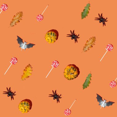 Cadılar Bayramı sembolleri desen kompozisyonu. Küçük balkabakları, sonbahar yaprakları, bahis, turuncu arka planda örümcek ve şeker. Asgari düşüş konsepti.