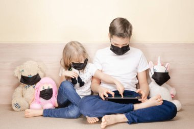 Erkek ve kız maskeler yüz maskesi takan oyuncaklar arasında tablet kullanıyorlar. COVID-19 koronavirüs salgını konsepti.