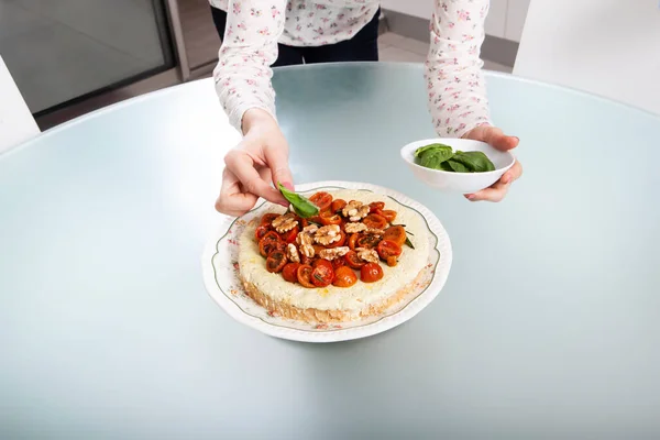 Bir kadının elleri ev yapımı sebzeli peynirli keki kirazlı domatesle süslüyor..